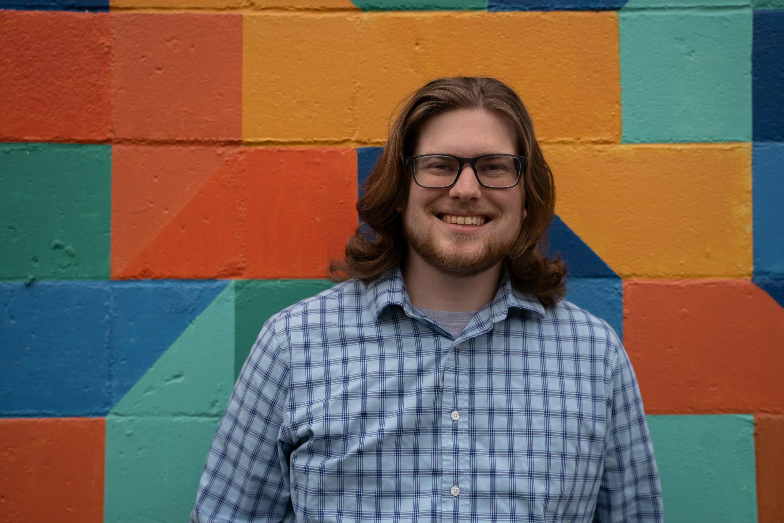 Young man standing in front of multicolored bricks smiling